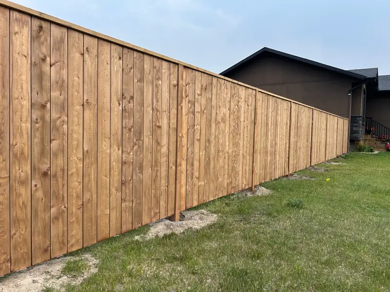 Freshly stained vertical-board wood privacy fence with a capped top rail beside a home in Saskatoon