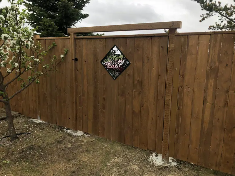 Stained wood privacy fence with a decorative wrought-iron diamond inlay and an arched post beam in Saskatoon