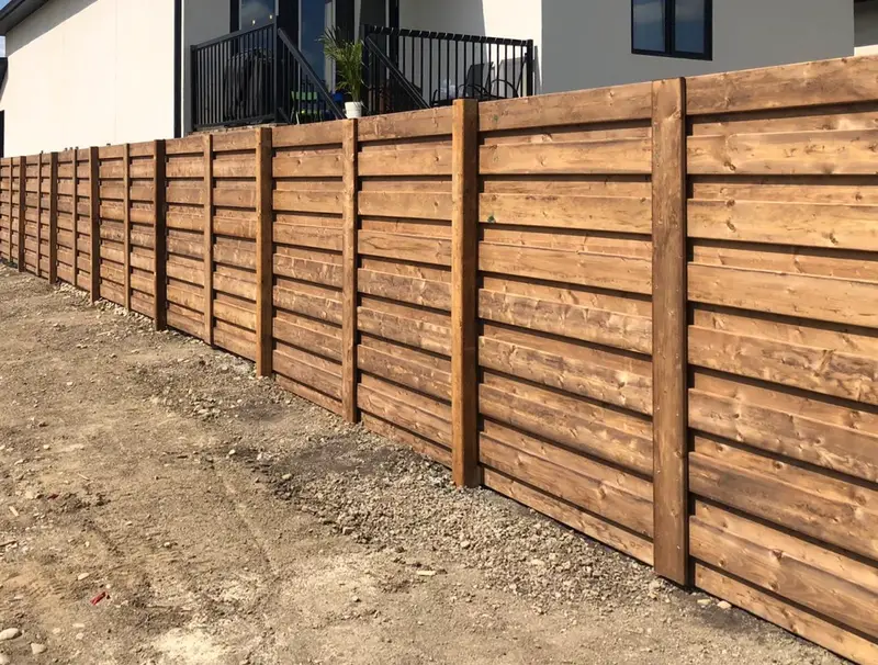 Modern horizontal-board wood fence with stained slats in front of a new home in Saskatoon